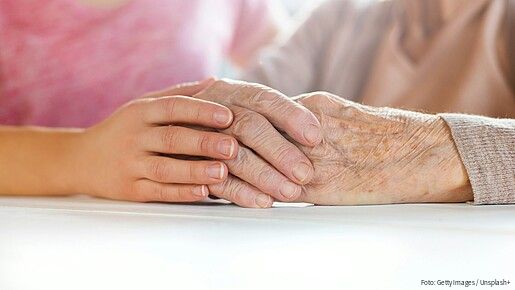 Foto einer jungen Hand, die eine ältere Hand umschließt.