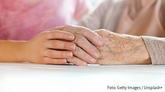 Foto einer jungen Hand, die eine ältere Hand umschließt.