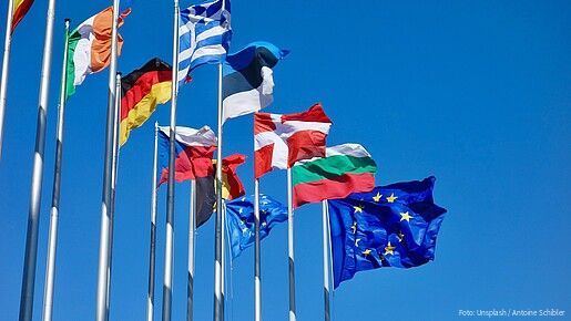 Verschiedene europäische Landesflaggen sowie eine EU-Flagge an Fahnenmasten wehen im Wind.