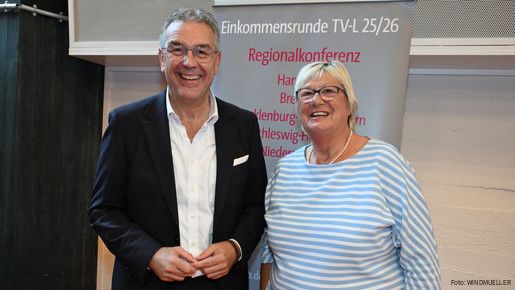 Ein Mann und eine Frau stehen vor einem grauen Aufsteller und blicken in die Kamera